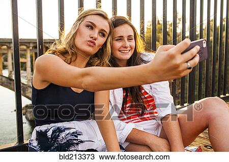 Stock Image - Caucasian teenage girls taking cell phone selfies. Fotosearch