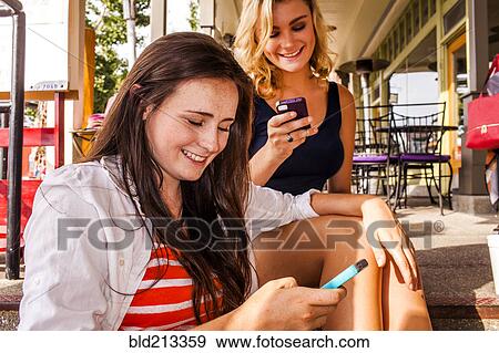Stock Photo - Caucasian teenage girls using cell phones in city. Fotosearch