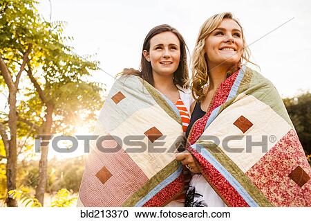 Stock Image - Caucasian teenage girls wrapped in blanket outdoors. Fotosearch