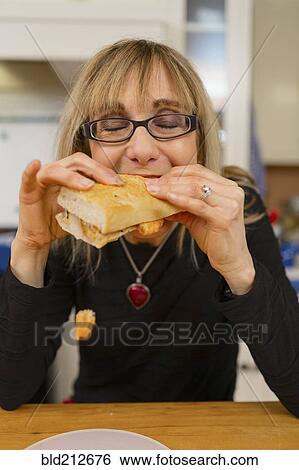 Stock Photograph - Caucasian woman eating sandwich in kitchen. Fotosearch