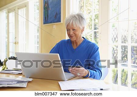 Stock Photo - Caucasian woman holding credit card and using laptop. Fotosearch