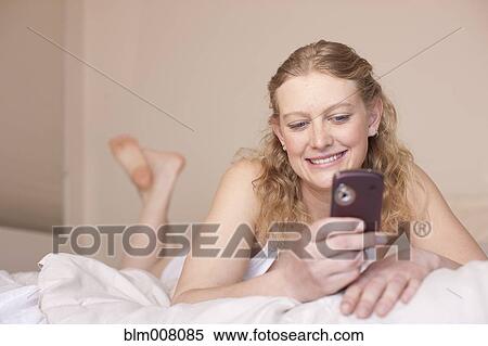 Stock Photography - Caucasian woman laying in bed using cell phone. Fotosearch