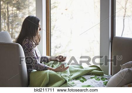 Stock Image - Caucasian woman meditating on sofa. Fotosearch