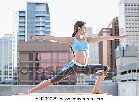 Stock Photo - Caucasian woman practicing yoga on urban rooftop. Fotosearch