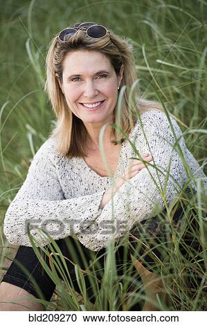 Stock Image - Caucasian woman sitting in tall grass. Fotosearch