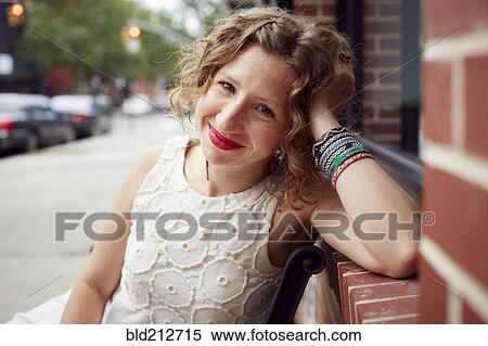 Stock Photography - Caucasian woman sitting on bench on city street. Fotosearch
