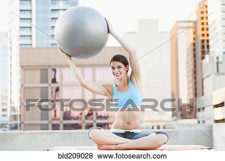 Stock Photo - Caucasian woman using fitness ball on urban rooftop. Fotosearch