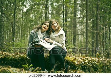 Picture - Caucasian women reading magazine in forest. Fotosearch