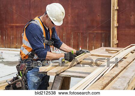 Stock Photo - Caucasian worker measuring wood at construction site. Fotosearch