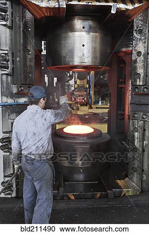 Stock Image - Caucasian worker operating steel melting machinery in factory. Fotosearch