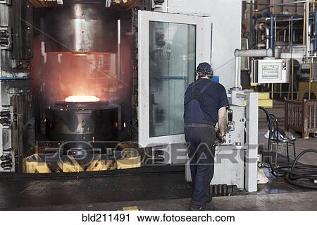 Stock Image - Caucasian worker operating steel melting machinery in factory. Fotosearch