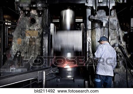 Stock Image - Caucasian worker operating steel melting machinery in factory. Fotosearch