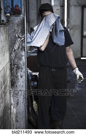 Stock Image - Caucasian worker wiping his face in factory. Fotosearch