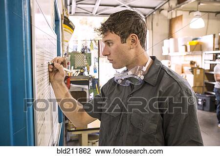 Stock Image - Caucasian worker writing on whiteboard in warehouse. Fotosearch