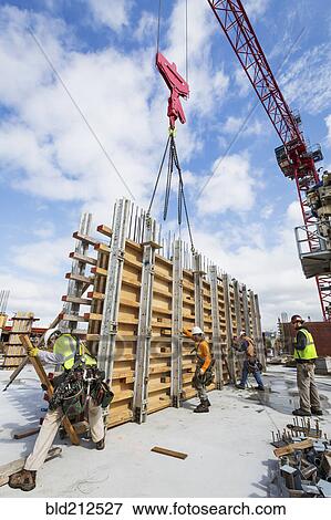 Stock Photo - Caucasian workers operating crane at construction site. Fotosearch