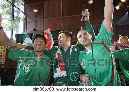 Stock Image - Cheering Hispanic men watching television in sports bar. Fotosearch