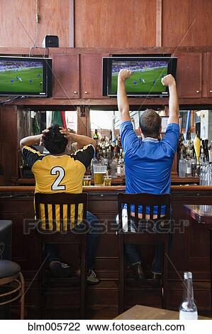 Cheering men watching television in sports bar View Large Photo Image Stock Image - Cheering men watching television in sports bar. Fotosearch