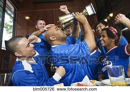 Stock Photograph - Cheering teammates and man drinking from trophy. Fotosearch