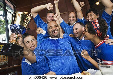 Cheering teammates and man holding trophy View Large Photo Image Stock Photograph - Cheering teammates and man holding trophy. Fotosearch