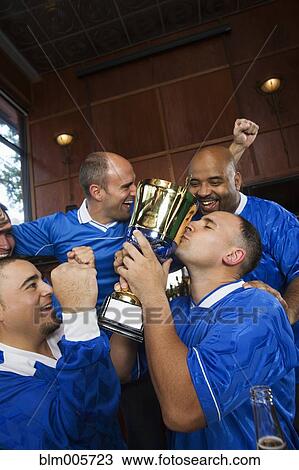 Stock Image - Cheering teammates and man kissing trophy. Fotosearch