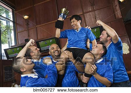 Stock Photo - Cheering teammates lifting man holding trophy. Fotosearch