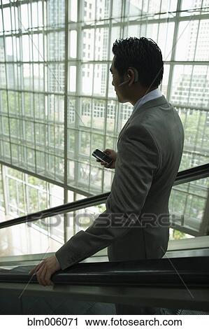 Chinese businessman holding cell phone on escalator View Large Photo Image Stock Image - Chinese businessman holding cell phone on escalator. Fotosearch