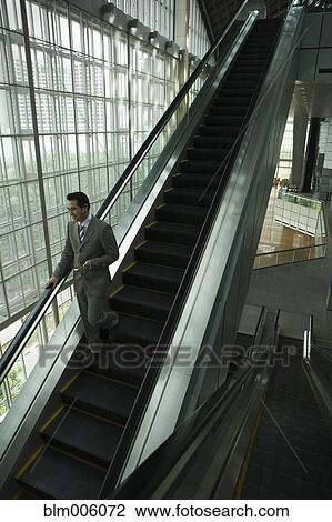 Chinese businessman holding cell phone on escalator View Large Photo Image Stock Image - Chinese businessman holding cell phone on escalator. Fotosearch
