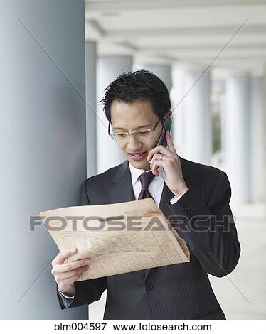 Chinese businessman reading newspaper and talking on cell phone View Large Photo Image Stock Photo - Chinese businessman reading newspaper and talking on cell phone. Fotosearch