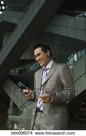 Picture - Chinese businessman talking on cell phone with hands-free device. Fotosearch