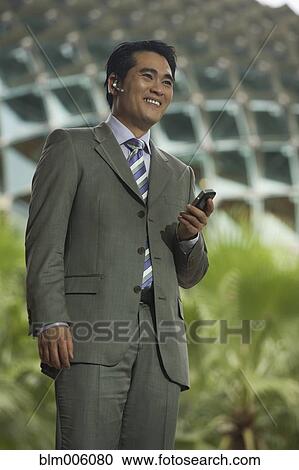 Stock Image - Chinese businessman talking on cell phone with hands-free device. Fotosearch