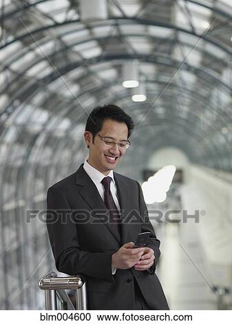 Stock Image - Chinese businessman text messaging on cell phone. Fotosearch