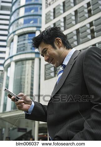 Stock Photo - Chinese businessman text messaging on cell phone. Fotosearch