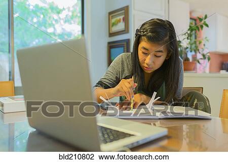 Stock Image - Chinese girl doing homework at table. Fotosearch