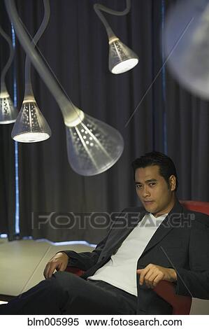 Stock Photography - Chinese man sitting in modern living room. Fotosearch
