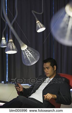 Stock Photograph - Chinese man text messaging with cell phone in living room. Fotosearch