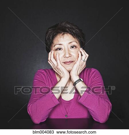 Stock Image - Close up of Asian woman with head in hands. Fotosearch