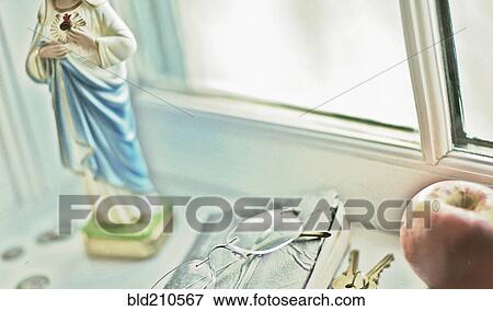 Stock Photo - Close up of glasses, religious statue and fruit on windowsill. Fotosearch