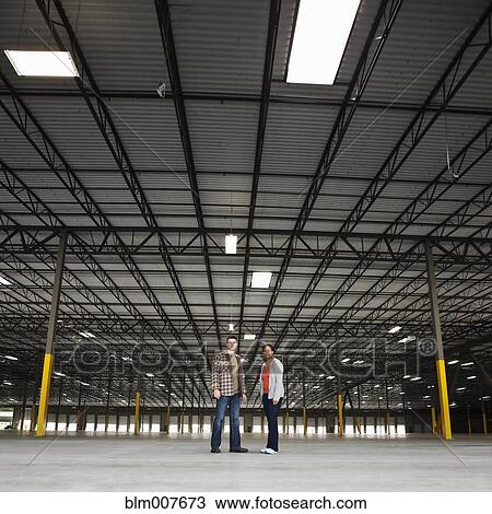 Stock Image - Co-workers standing in empty warehouse. Fotosearch