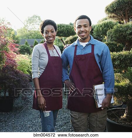 Stock Image - Co-workers working in garden nursery. Fotosearch