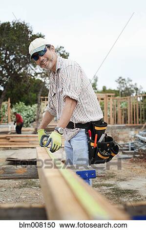 Stock Image - Construction worker measuring lumber. Fotosearch