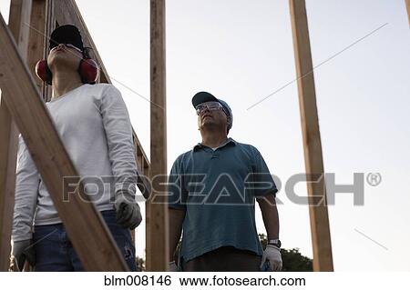 Construction workers assembling house frame View Large Photo Image Stock Photograph - Construction workers assembling house frame. Fotosearch