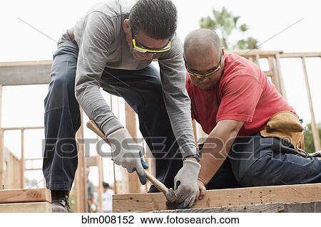 Stock Image - Construction workers building house frame. Fotosearch