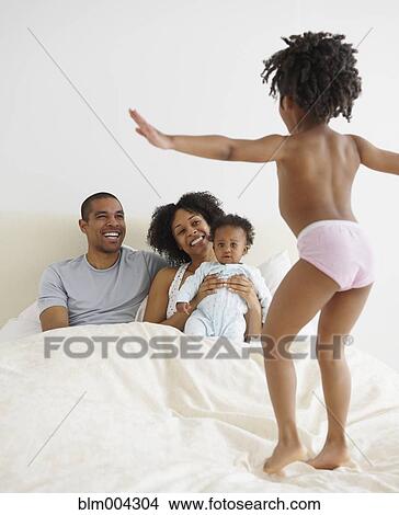 Couple and baby watching girl jump on bed View Large Photo Image Picture - Couple and baby watching girl jump on bed. Fotosearch