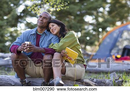 Couple camping and sitting on log View Large Photo Image Stock Image - Couple camping and sitting on log. Fotosearch