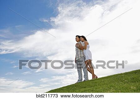 Stock Image - Couple hugging on grassy hillside. Fotosearch