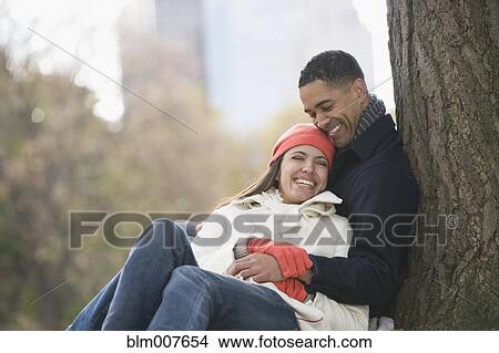 Picture - Couple leaning against tree in park. Fotosearch