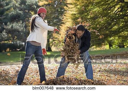 Couple playing in autumn leaves in park View Large Photo Image Stock Photo - Couple playing in autumn leaves in park. Fotosearch