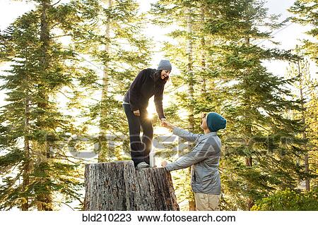 Stock Image - Couple playing on tree stump in forest. Fotosearch