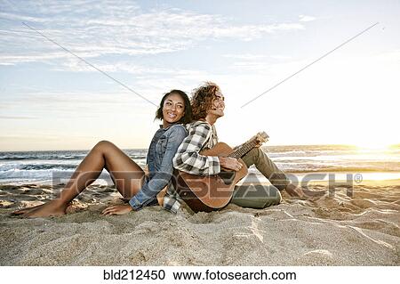 Stock Image - Couple relaxing together on beach. Fotosearch