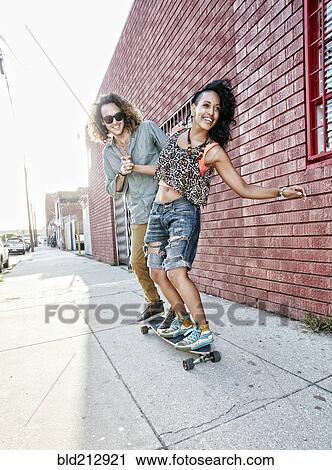 Stock Image - Couple riding skateboard on city street. Fotosearch